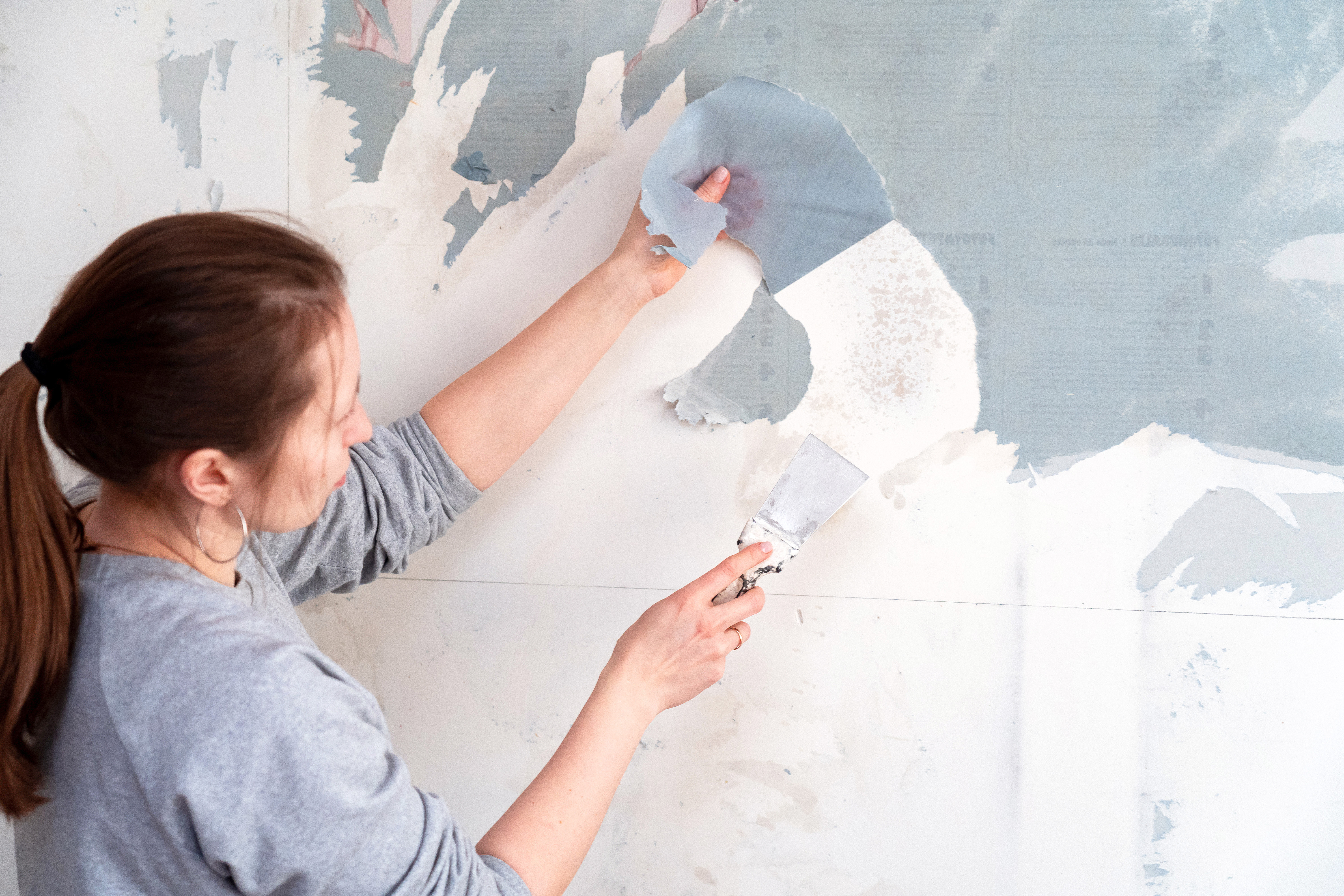 Woman using a scraper to remove wallpaper from the wall