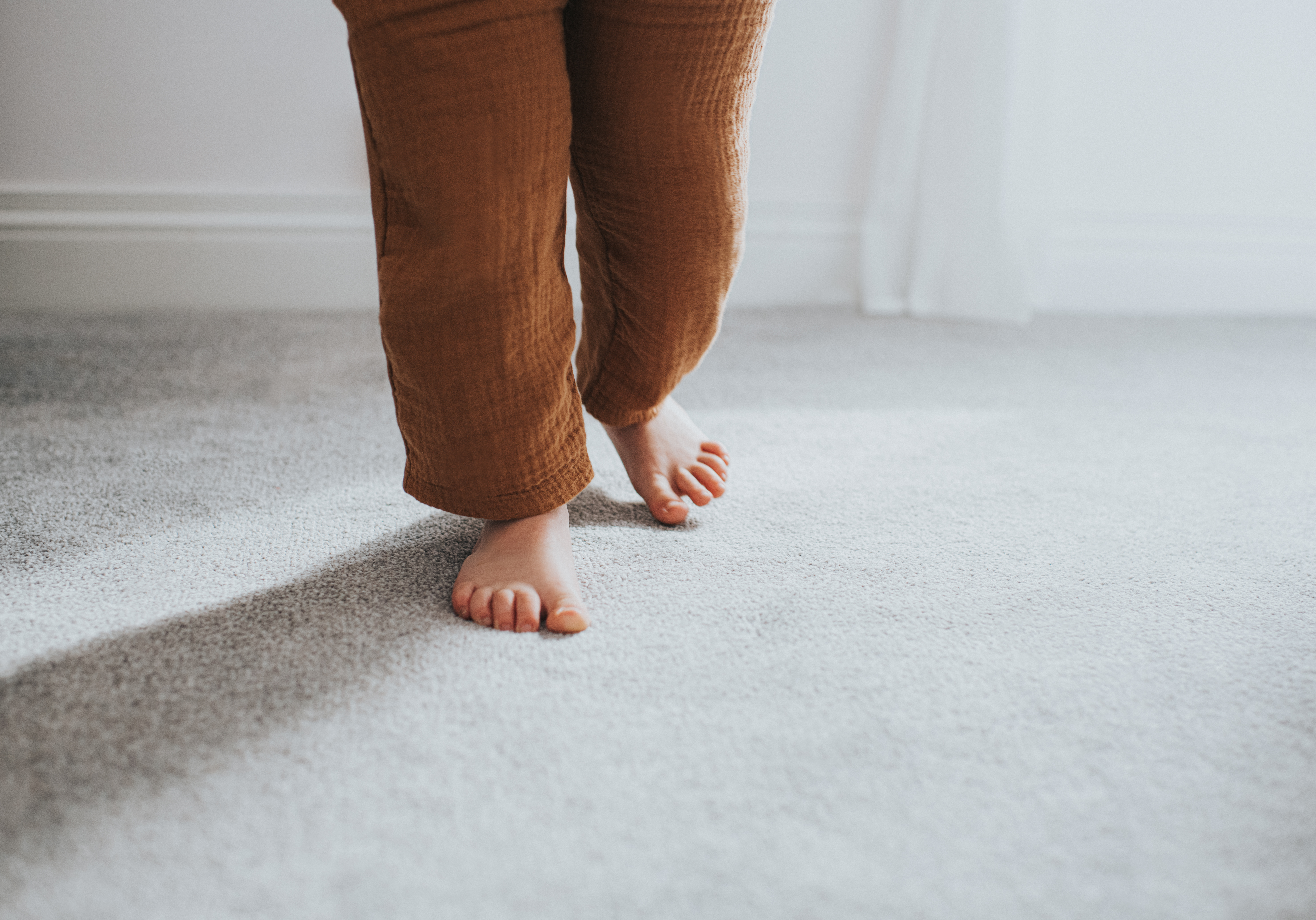 A toddler walking barefoot on gray carpet 