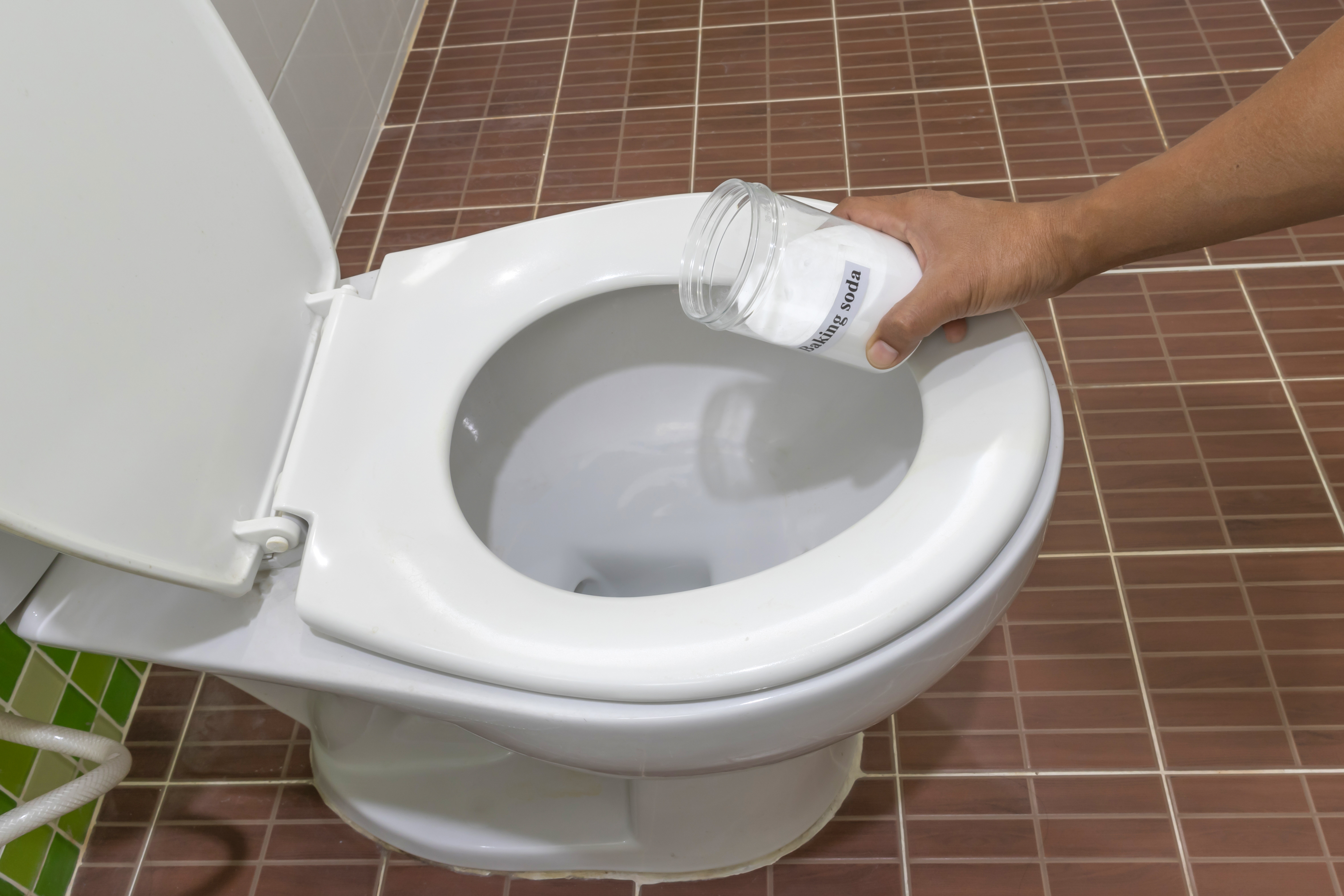 A person pouring baking soda on a toilet