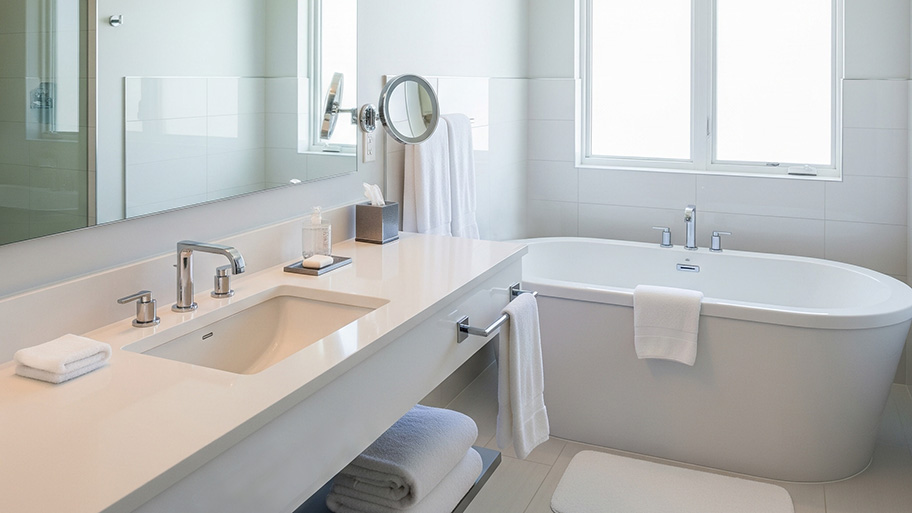 A bright, modern bathroom features a white freestanding tub next to a vanity with a single sink