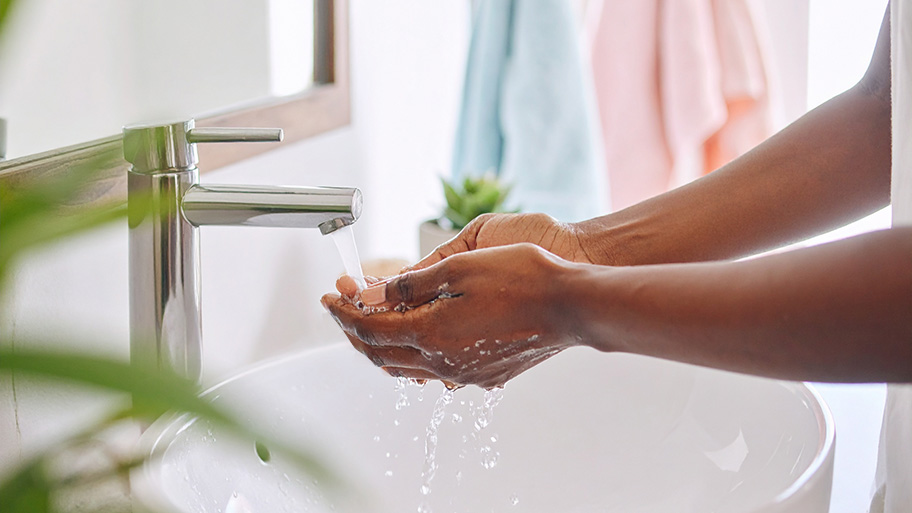 A person washes their hands in a white sink under running water from a modern chrome faucet