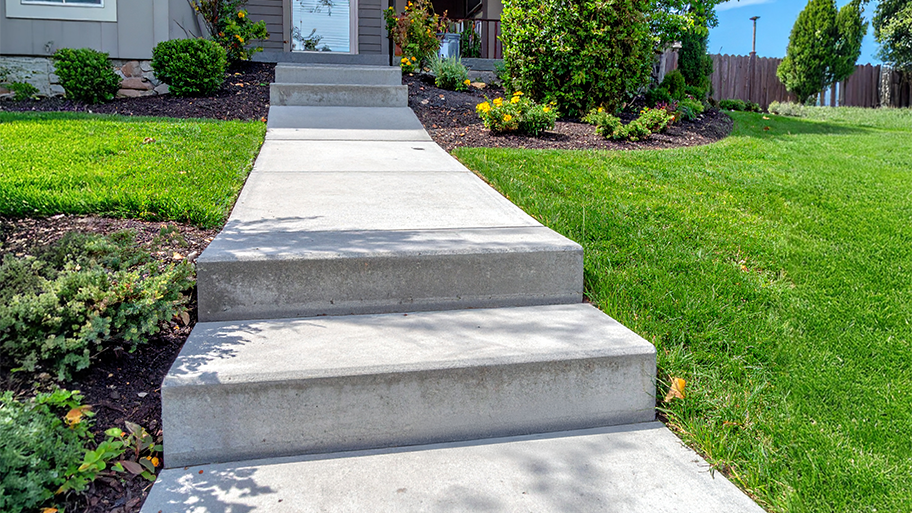 Concrete steps lead up a landscaped front yard to a home's entrance, bordered by grass and flower beds