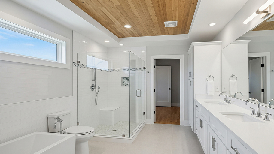 A spacious white bathroom with a glass shower, a soaking tub, and a wooden plank ceiling with a fan and recessed lighting.