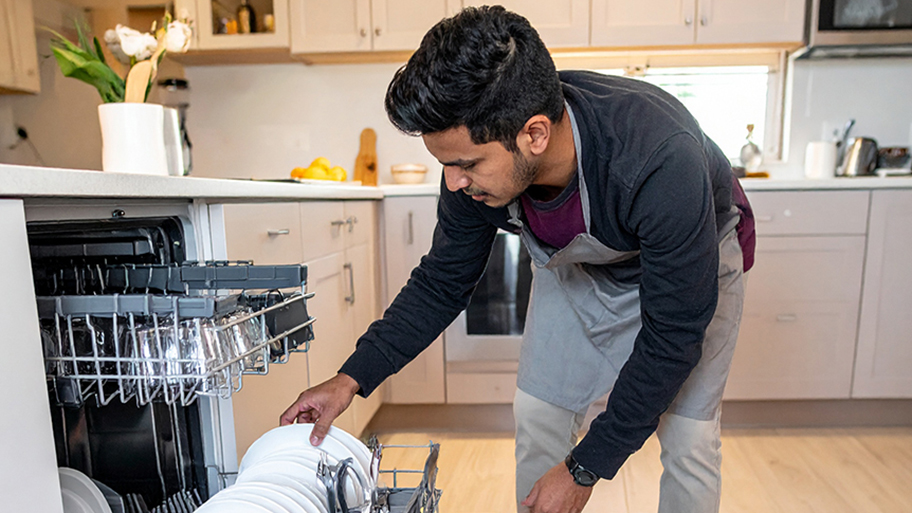 Man unloading clean plates from a dishwasher rack in a bright modern kitchen.