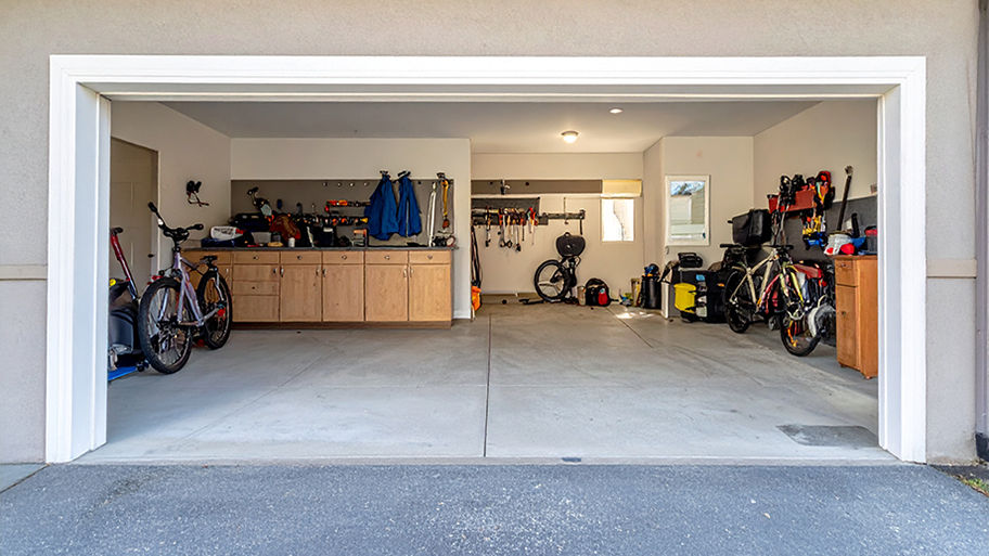 A well-organized two-car garage with a concrete floor, built-in cabinets, a workbench, and various tools and bicycles.