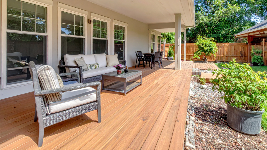 A spacious backyard deck with outdoor seating, wood flooring, and a covered patio overlooking a landscaped garden.