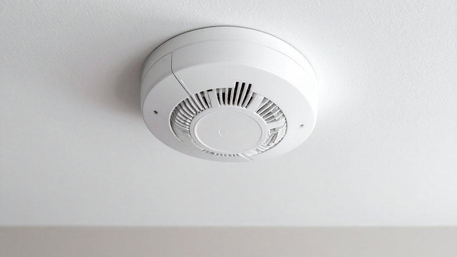 A white smoke detector is mounted on a ceiling in a modern home for fire and safety protection.