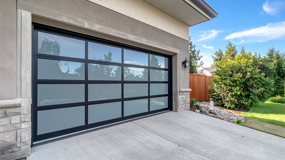 A modern garage with a frosted glass and black metal door set in a stucco and stone exterior