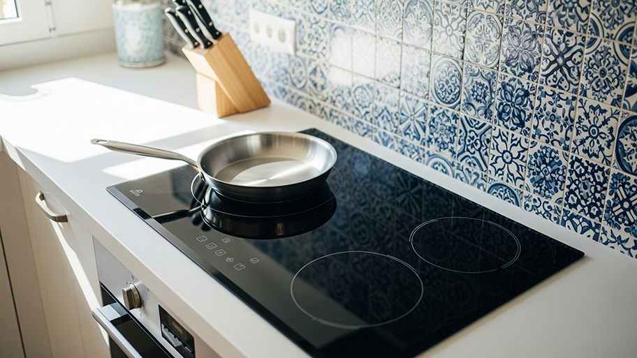 A close-up of a modern electric glass stovetop with a pan on a burner and a blue patterned tile backsplash