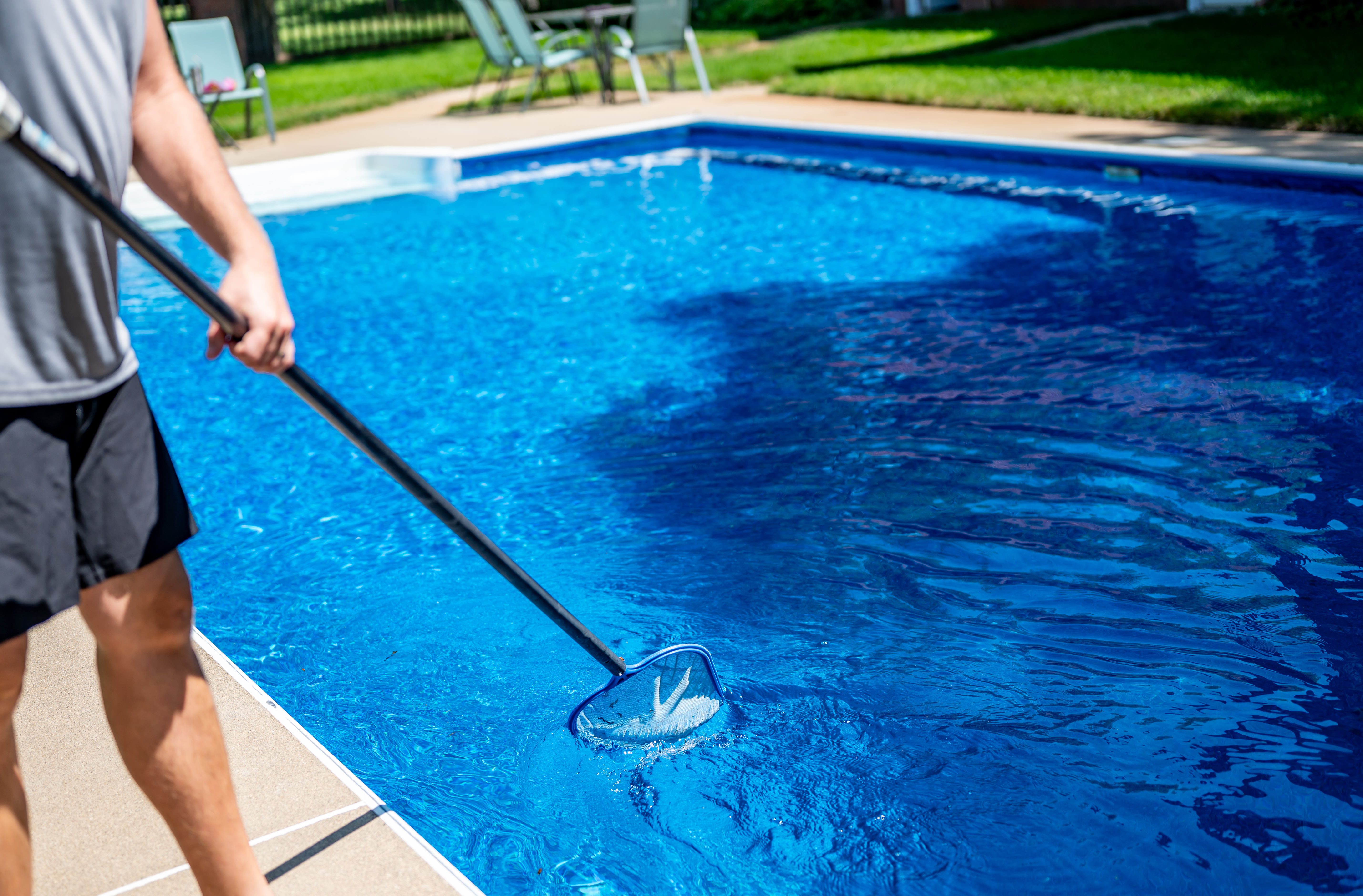 man using skimmer to clean pool