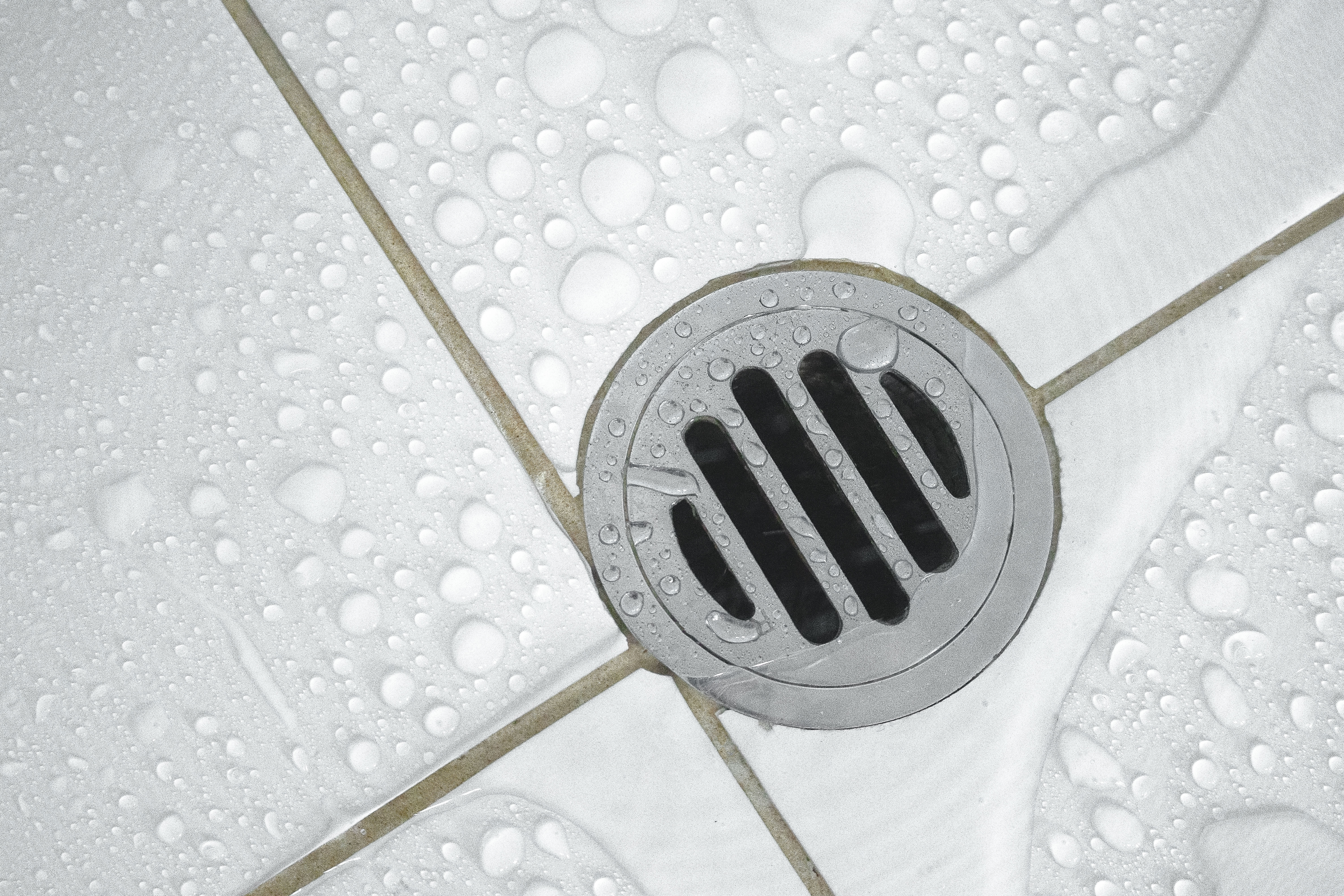 Wet shower floor with white tile and a round drainage cover 