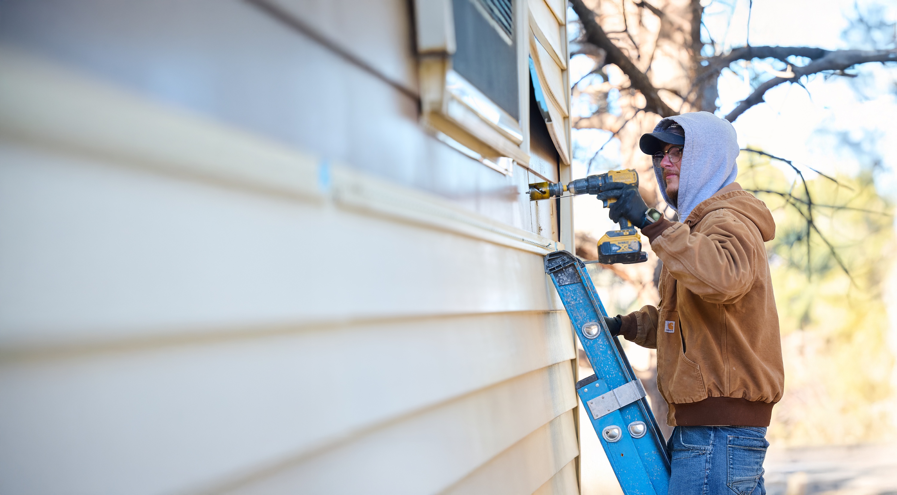 A contractor installs insulation on the exterior of a home using a power drill.