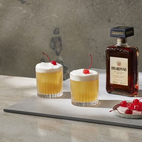 Disaronno Sour med en flaska Disaronno i bakgrunden