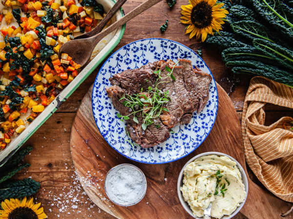 Entrecôte på vitblå tallrik, tärnade rotfrukter i panna och vispar kryddsmöt i vit skål.