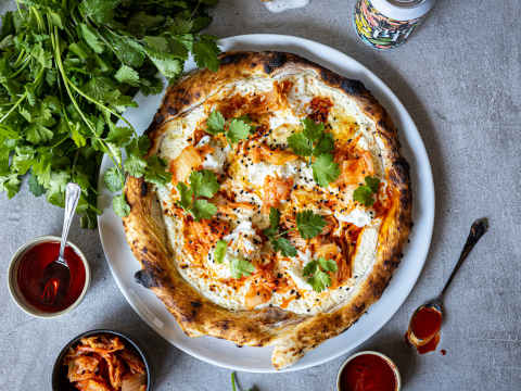 Pizza med kimchi på ett bord med koriander och srirachasås