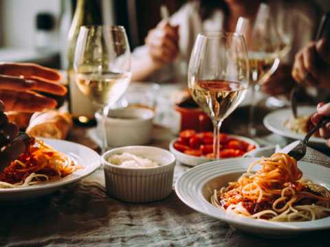 Middagsbjudning med pasta i tomatsås och vitt vin i glas på bord