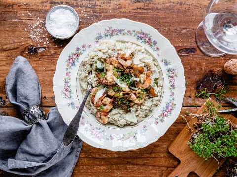 Risotto med räkor på vit tallrik på träbord.