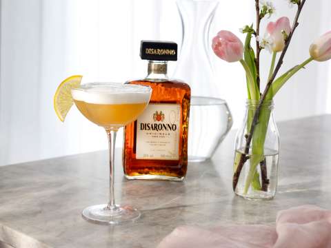 Disaronno Sour med en flaska Disaronno i bakgrunden
