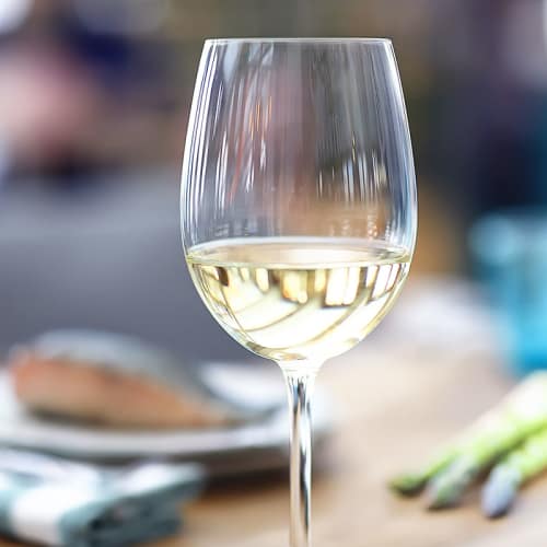 Rieslingvin i ett glas med fiska och sparris i bakgunden.