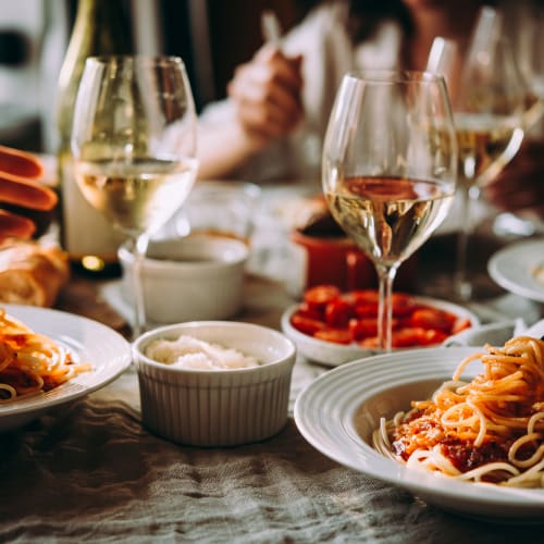 Middagsbjudning med pasta i tomatsås och vitt vin i glas på bord.