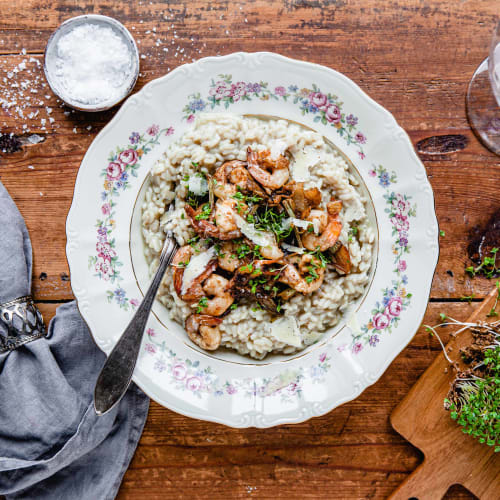 Risotto med räkor på vit tallrik på träbord.