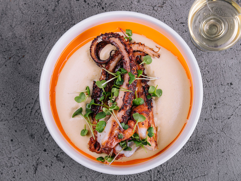 Grillad bläckfisk på en tallrik med ett glas vitt vin bredvid.