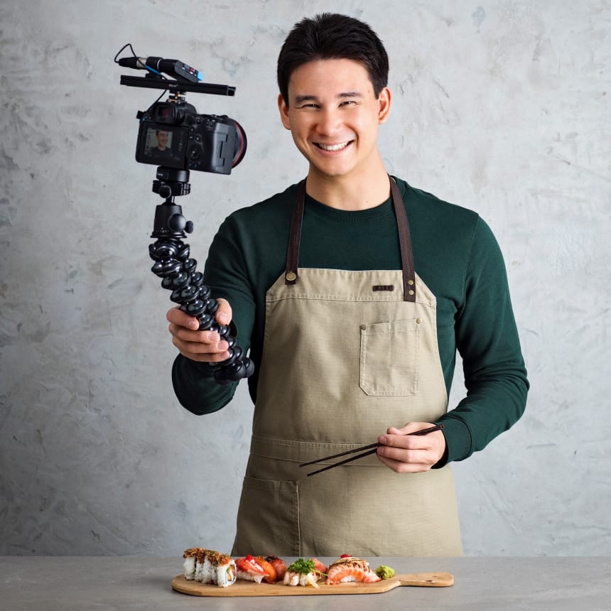 Filip Poon med förkläde hållandes i kamera och men en sushibricka framför sig på en stenbänk.