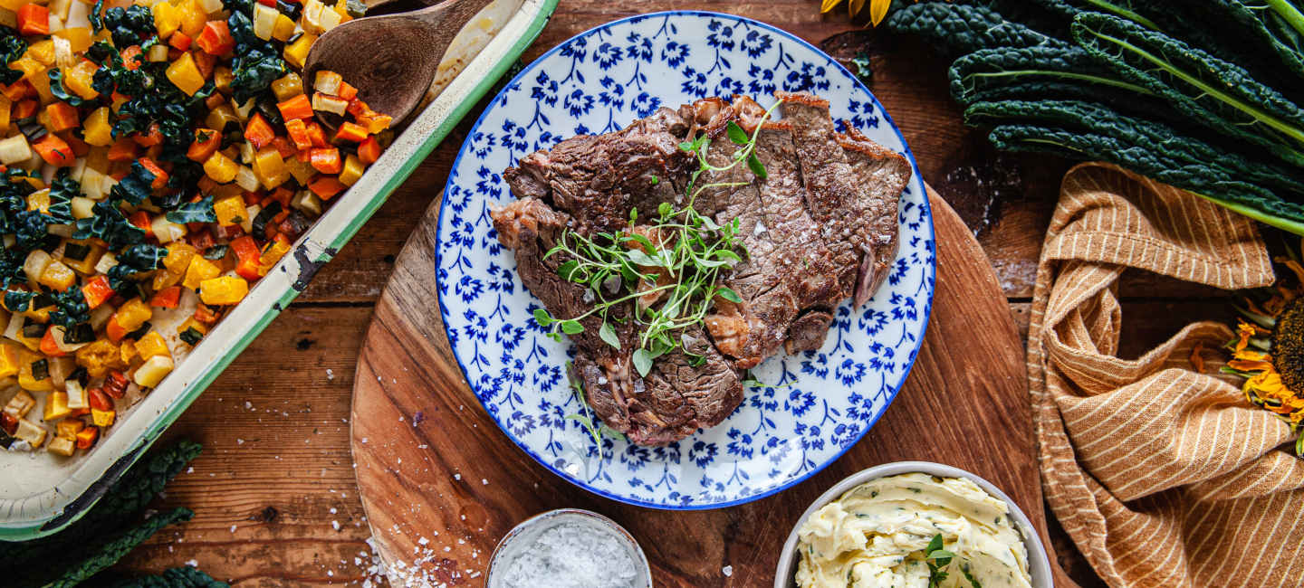 Entrecôte på vitblå tallrik, tärnade rotfrukter i panna och vispar kryddsmöt i vit skål.