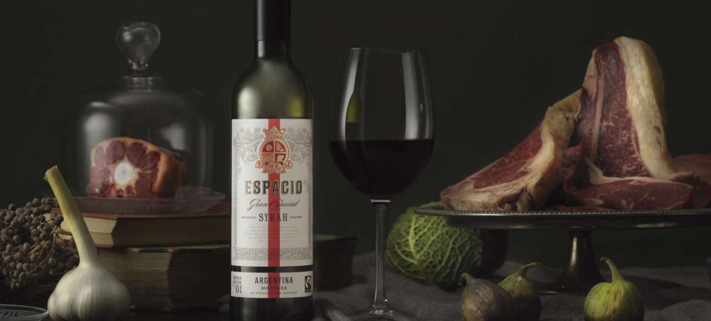 Espacio Syrah på bord med glas, kött och grönsaker.