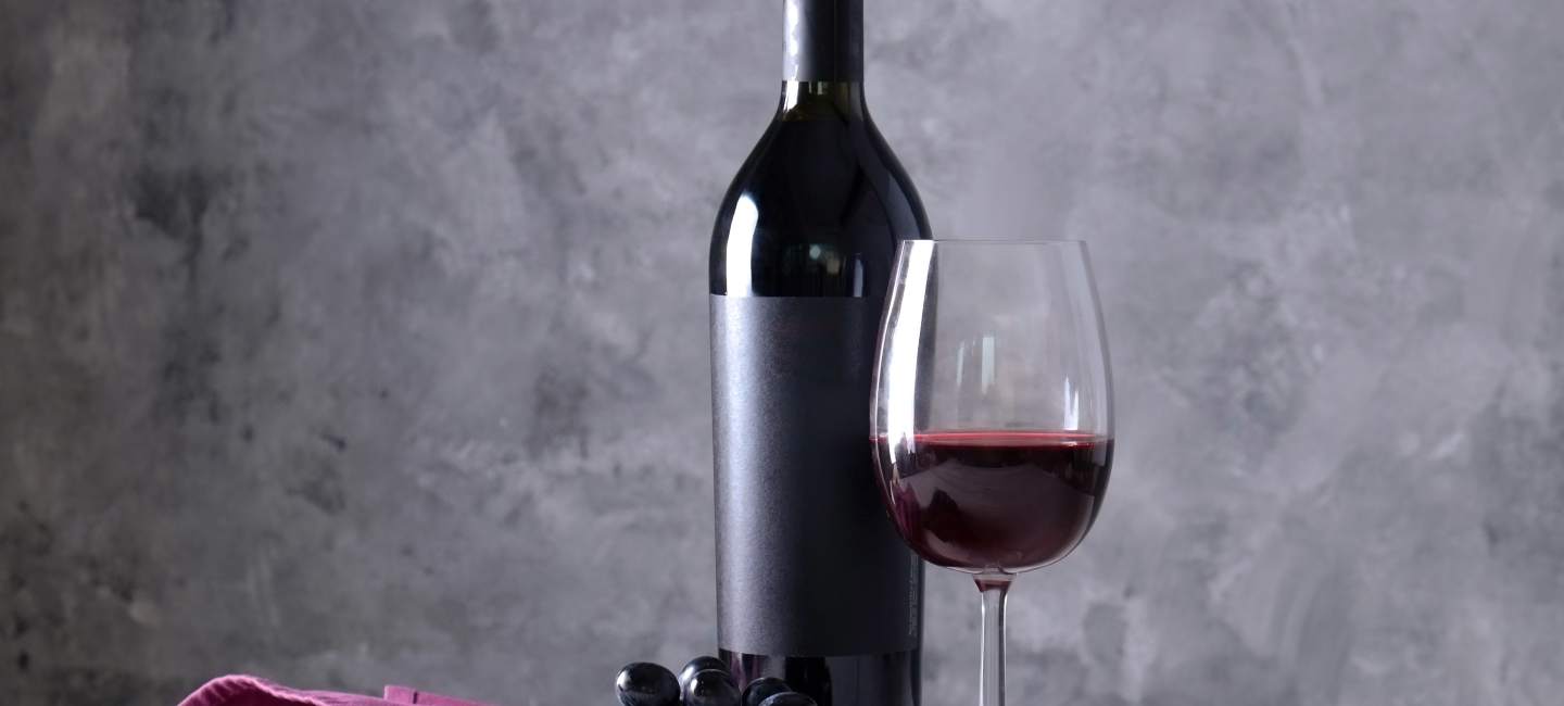 Cabernet Sauvignon på flaska, i vinglas och sin druvklase med grå bakgrund.