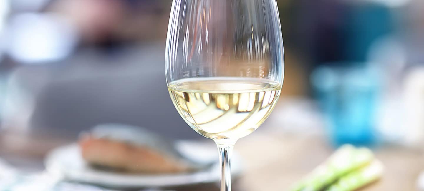 Rieslingvin i ett glas med fiska och sparris i bakgunden.