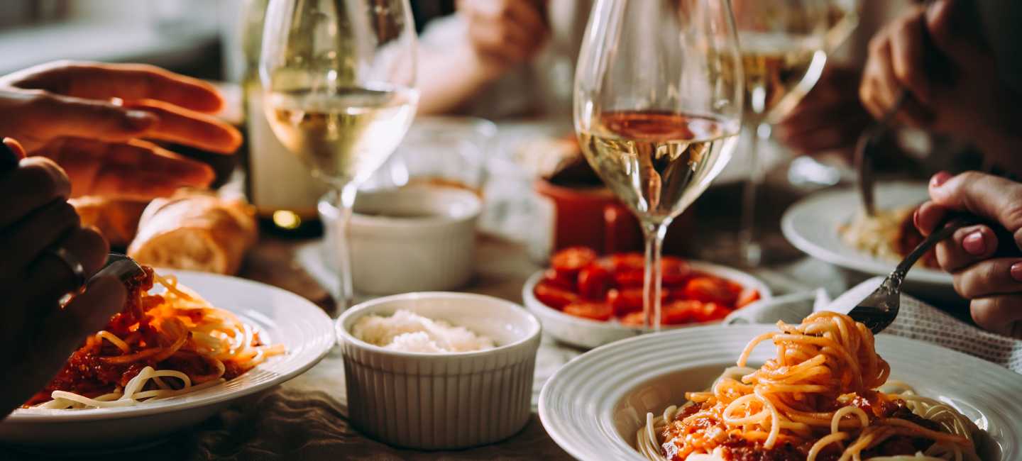 Middagsbjudning med pasta i tomatsås och vitt vin i glas på bord