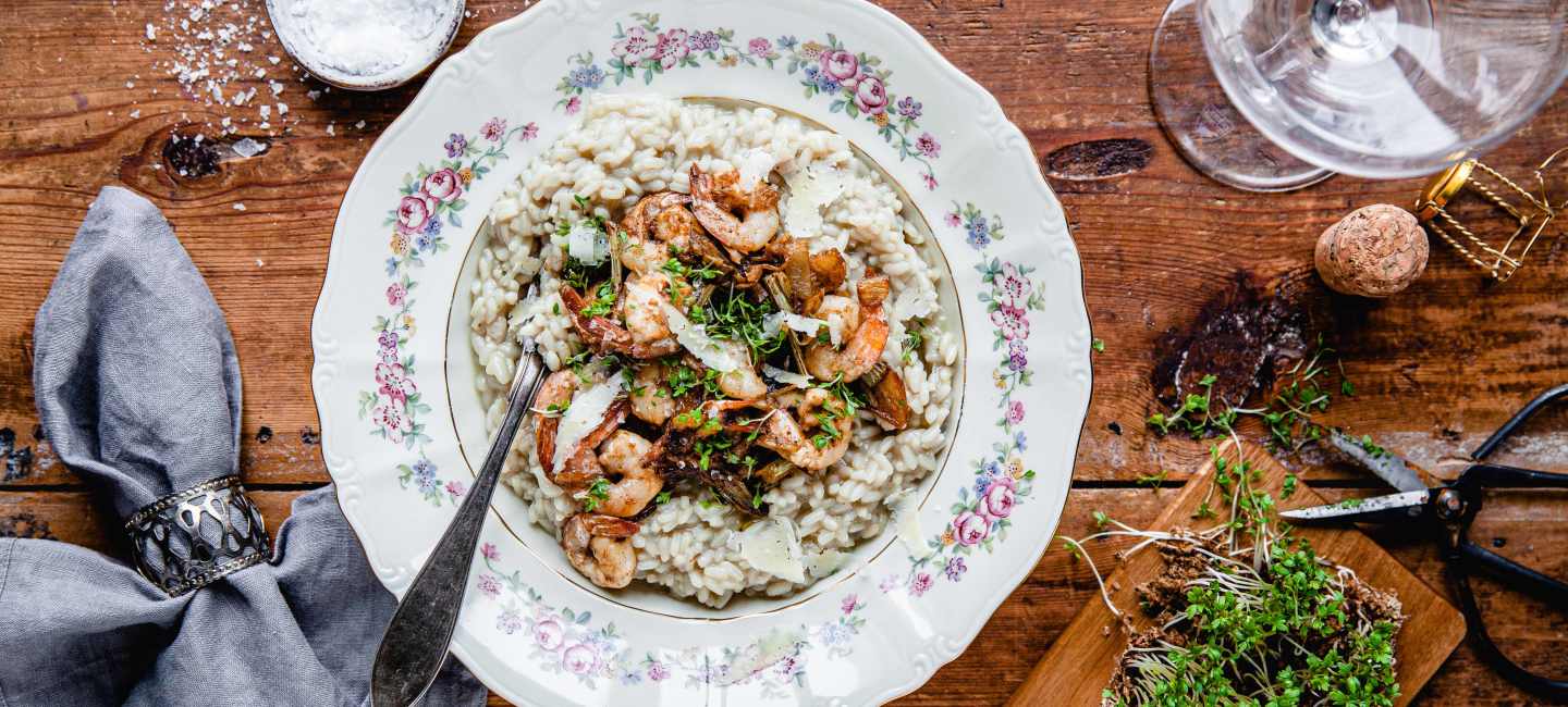 Risotto med räkor på vit tallrik på träbord.