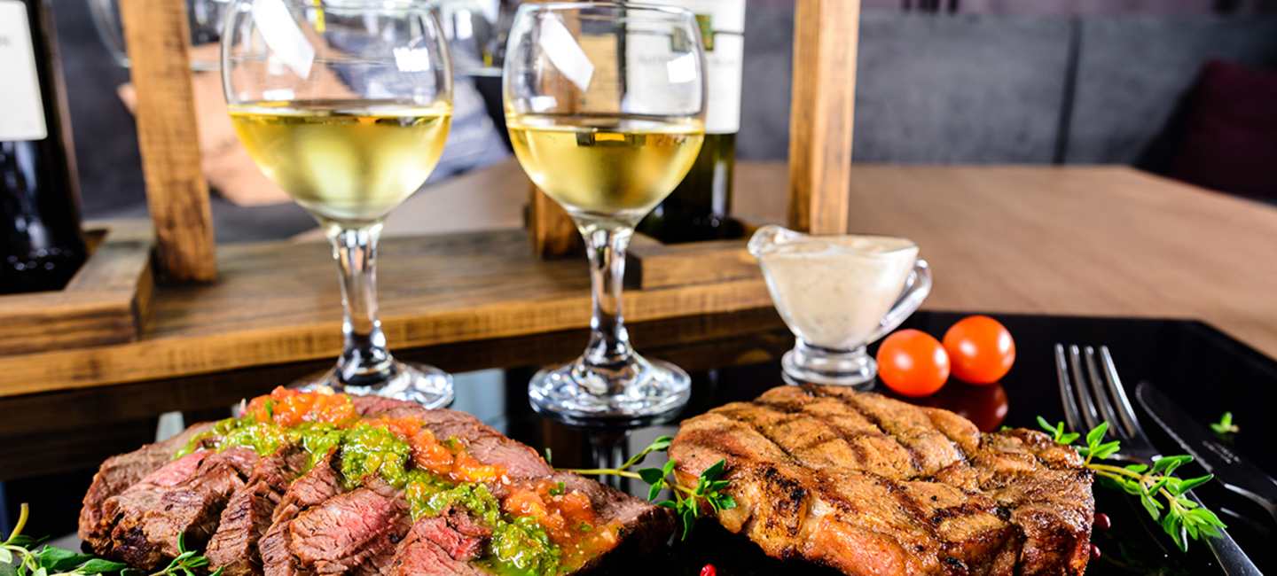 Två tallrikar med kött och två glas vitt vin 