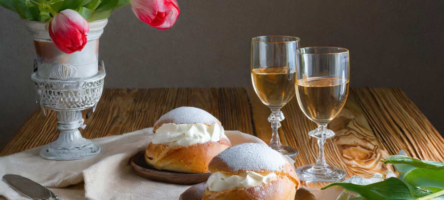 Två semlor på ett träbord med två glas dessertvin och några tuulpaner.
