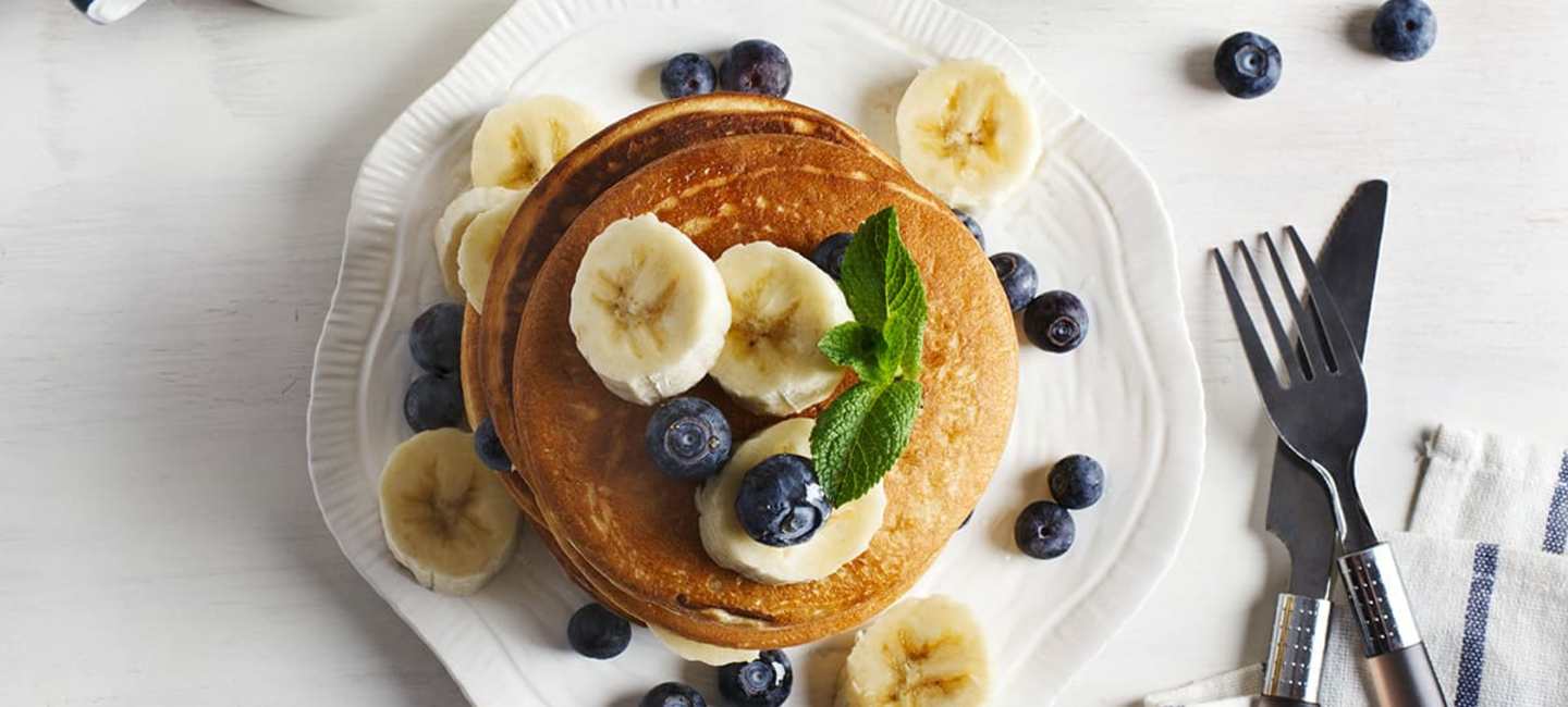 Veganska bananpannkakor med bananskivor och blåbär på vit tallrik.