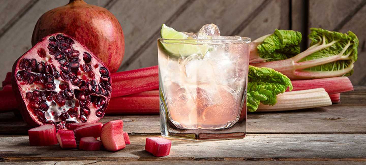 Ett rosa cocktailglas med rabarber och granatäpple bredvid 