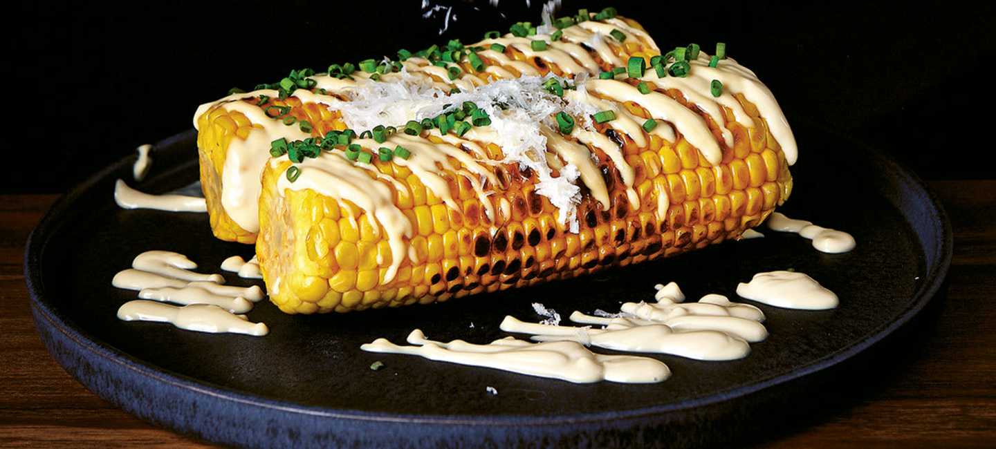 två grillade majskolvar på svart fat 
