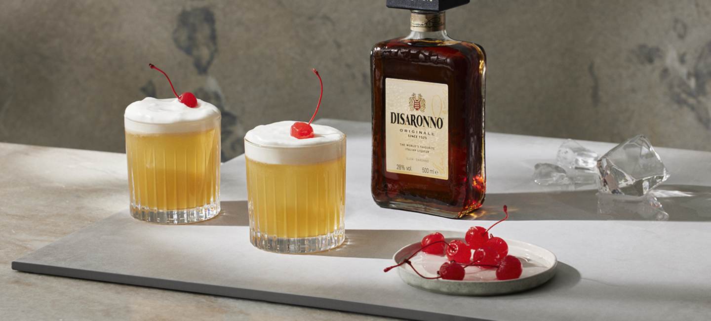 Disaronno Sour med en flaska Disaronno i bakgrunden