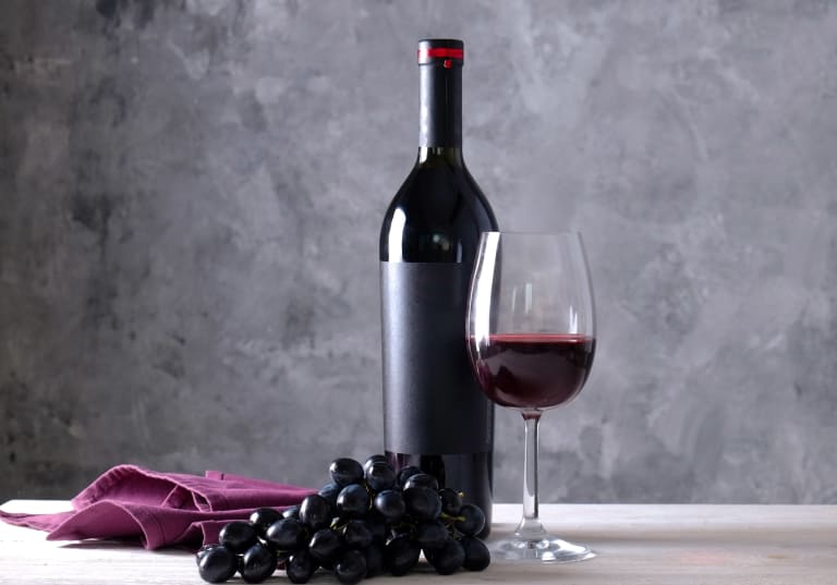 Cabernet Sauvignon på flaska, i vinglas och sin druvklase med grå bakgrund.
