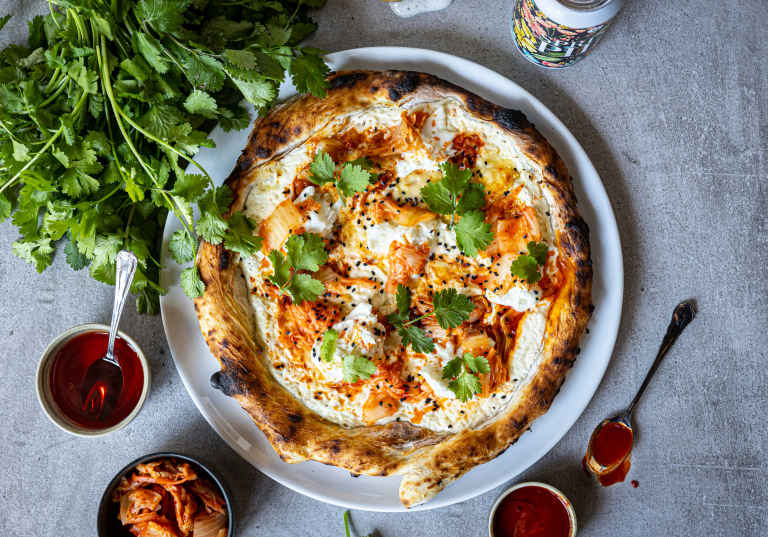 Pizza med kimchi på ett bord med koriander och srirachasås