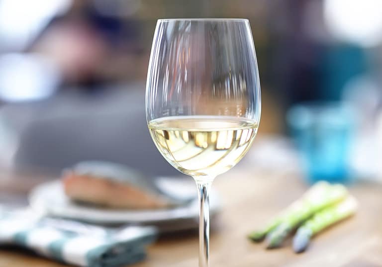Rieslingvin i ett glas med fiska och sparris i bakgunden.