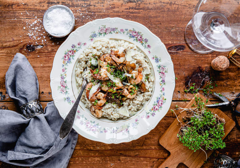 Risotto med räkor på vit tallrik på träbord.