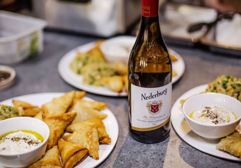 Samosas med makrill och yoghurtsås på ett bord, samt en vinflaska från Nederburg.