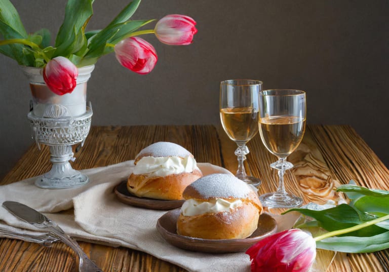 Två semlor på ett träbord med två glas dessertvin och några tuulpaner.