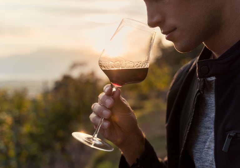 Man som doftar på vin i ett vinglas på en vingård.