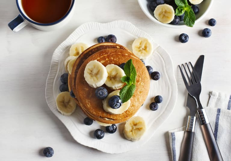 Veganska bananpannkakor med bananskivor och blåbär på vit tallrik.