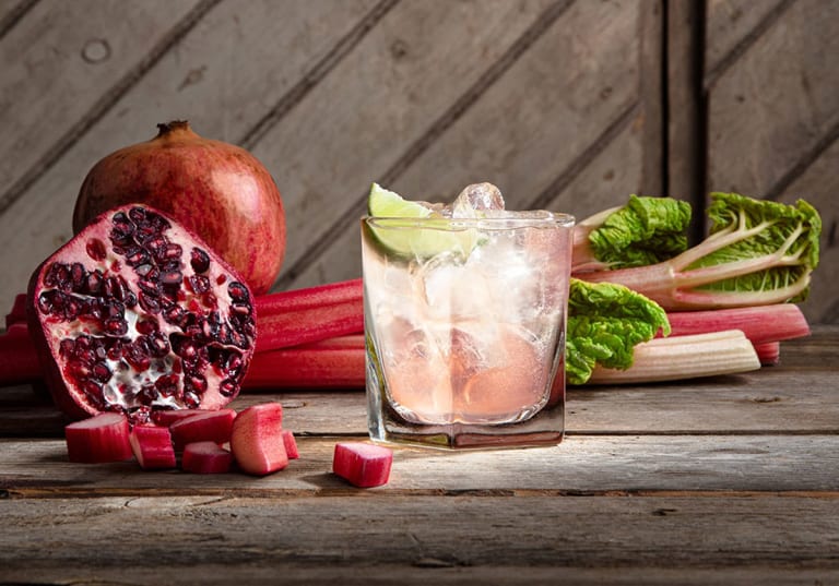 Ett rosa cocktailglas med rabarber och granatäpple bredvid 