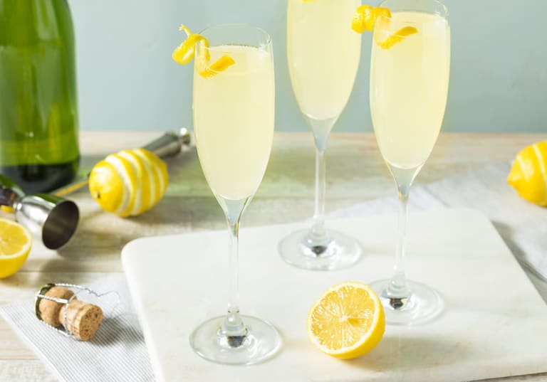 Tre champagneglas med gul drink på bord 