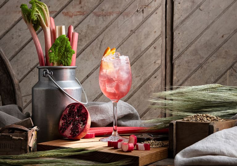 Vinglas med rosa drink med rabarber och grantäpple intill 